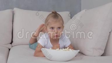 一个小女孩在软榻上吃着爆米花，看着电<strong>视屏</strong>幕。